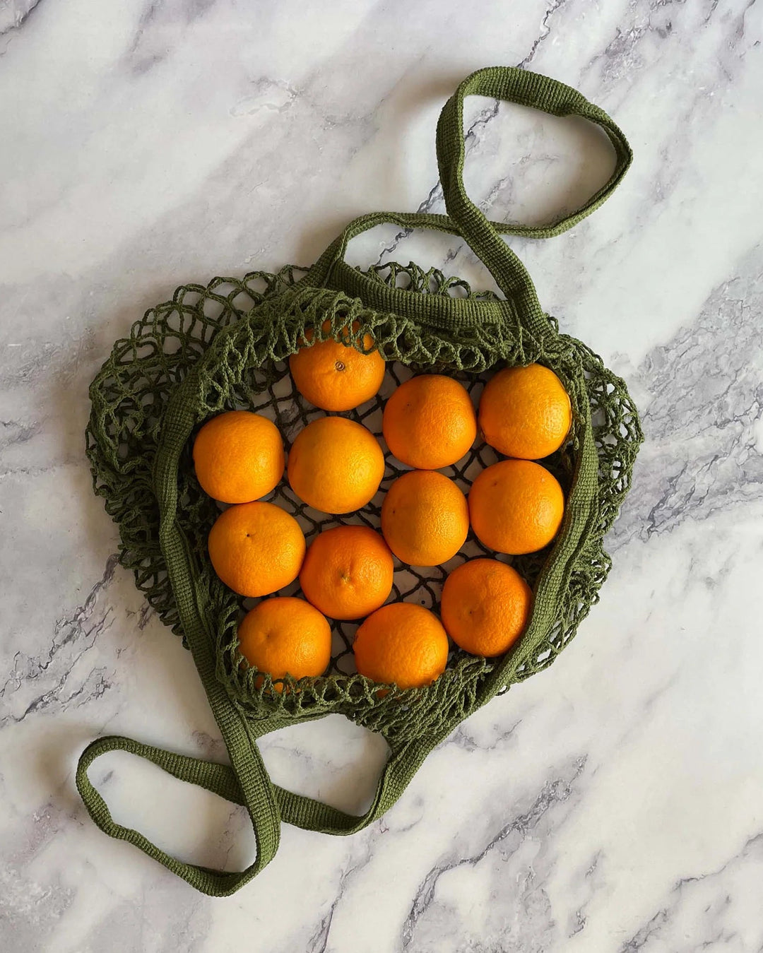Green mesh bag filled with oranges on a marble surface