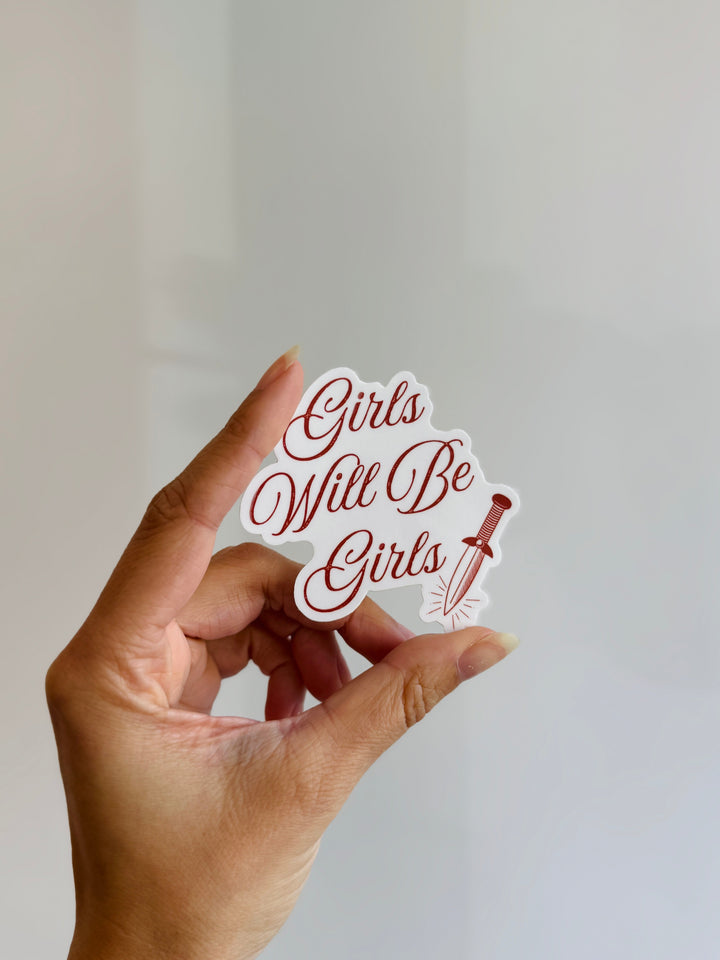 A hand holds a die-cut sticker that reads &