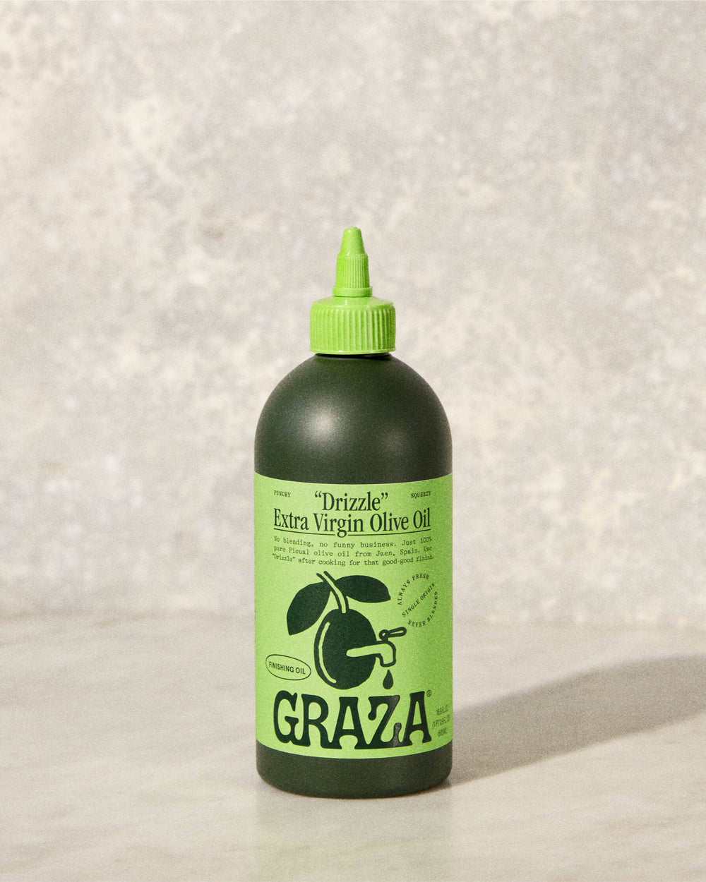 Green bottle of GRAZA olive oil on a textured white background