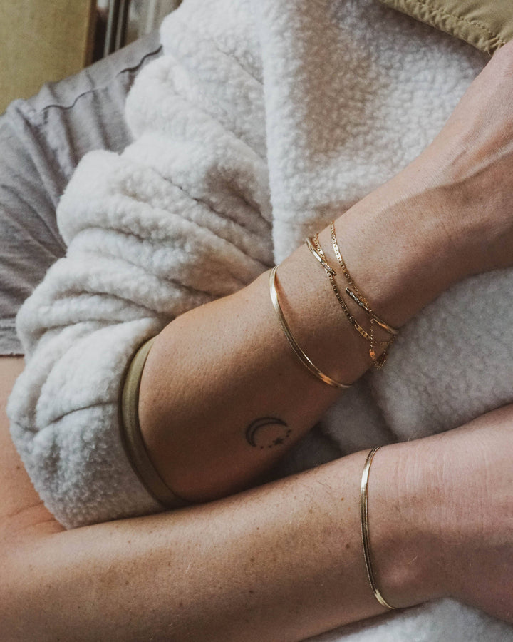 Person wearing gold bracelets on an arm with a neutral background
