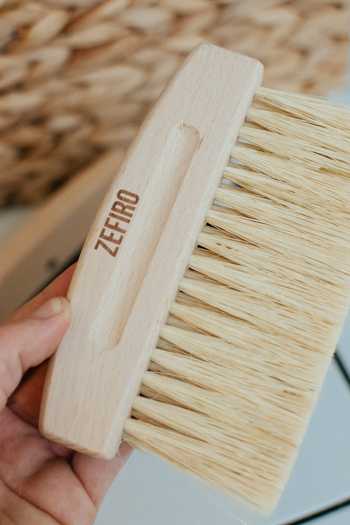 Wooden brush with bristles held by a hand, brand 'Zefiro' visible.