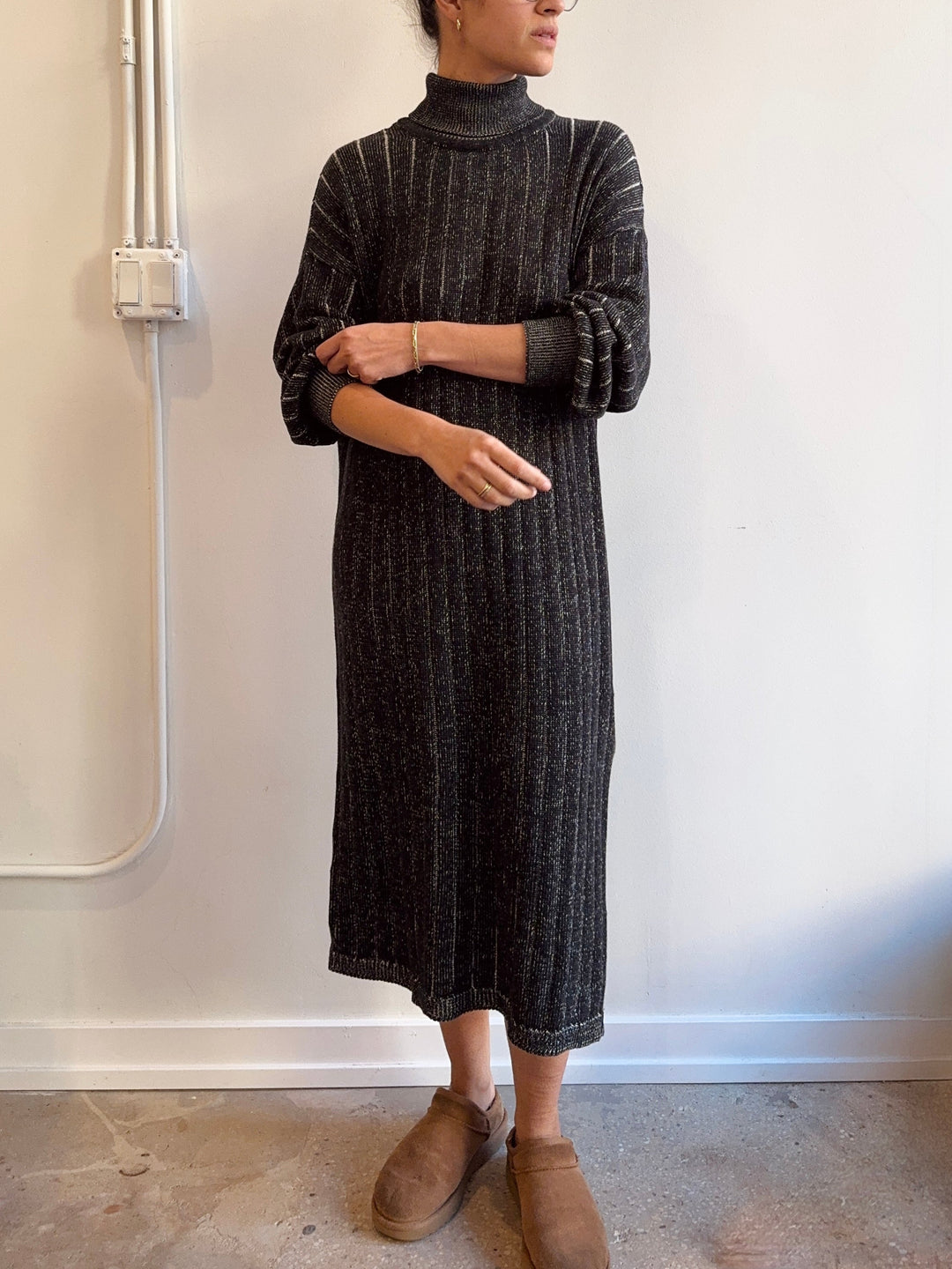 Person wearing a dark ribbed knit dress against a white wall.