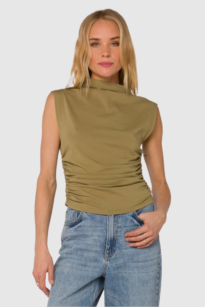 Woman wearing a green mock neck sleeveless top and blue jeans on a white background