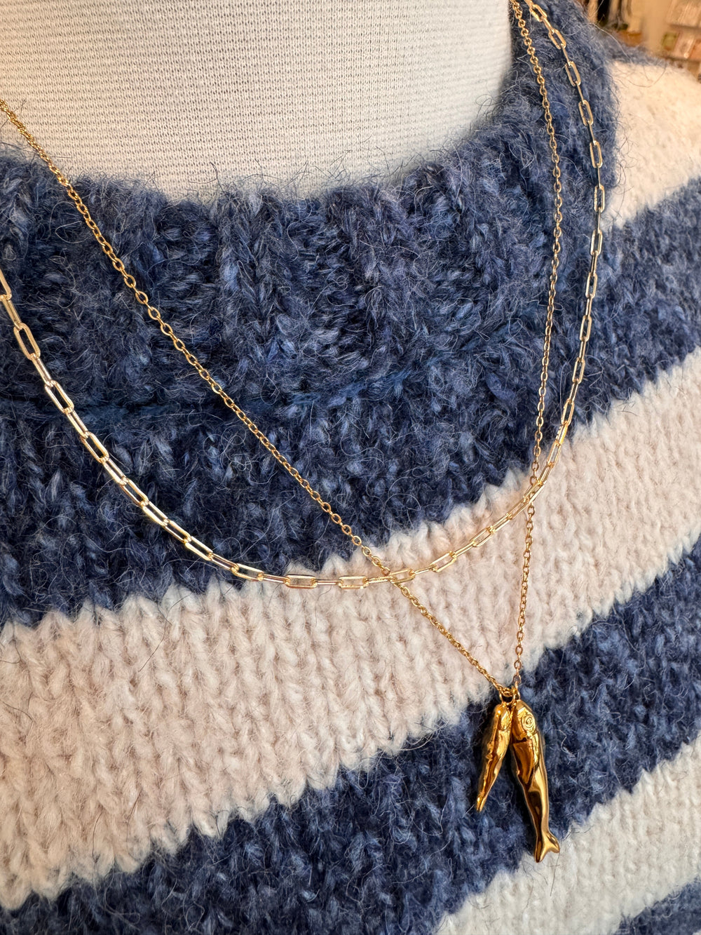 Gold chain necklace with a fish pendant on a blue and white striped fabric background
