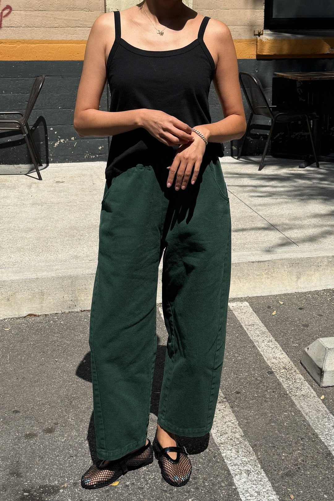 Person wearing a black tank top and green pants standing on a street.