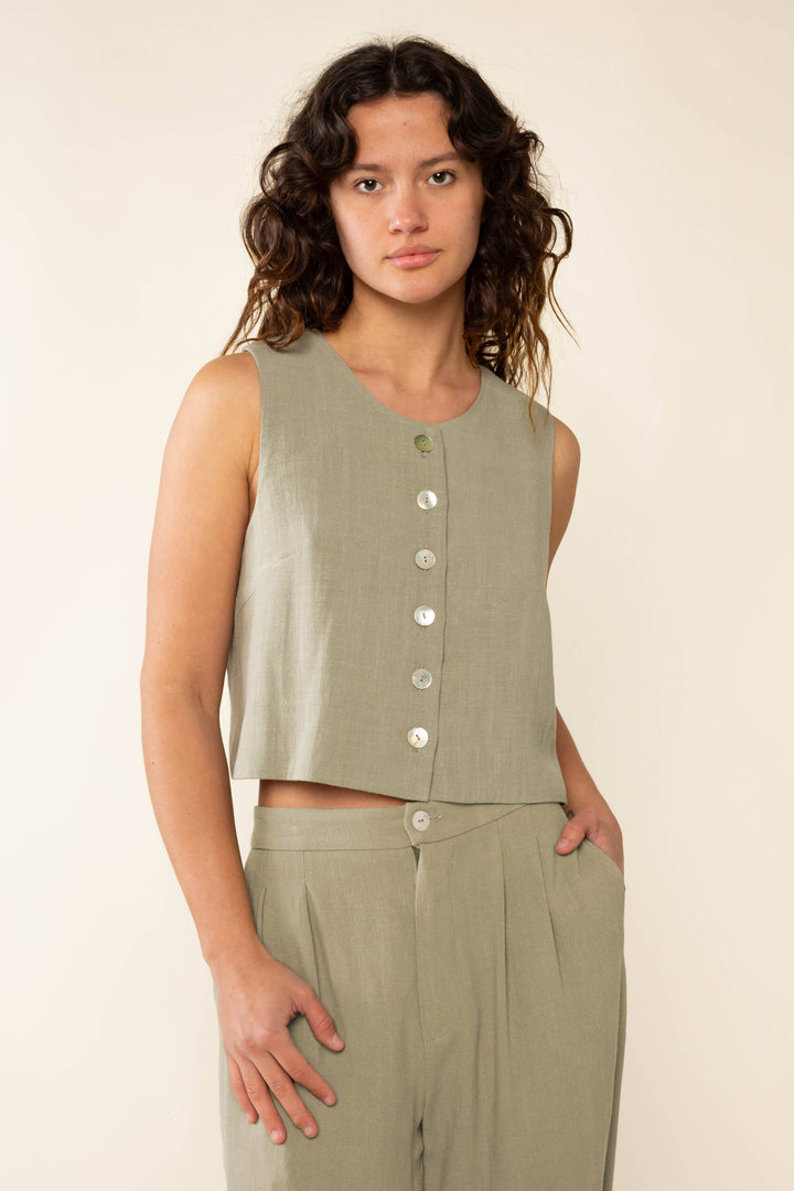 Woman wearing a sleeveless green top with buttons on a plain background