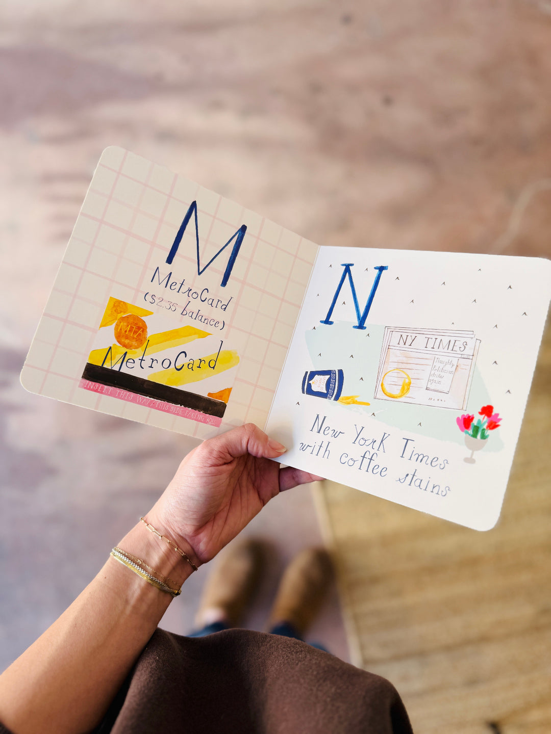 Hand holding two cards with illustrations and text, one labeled 'MetroCard' and the other with 'New York Times with coffee shops'.