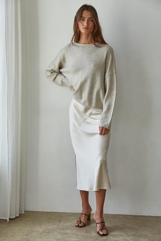 Woman wearing a light gray sweater and white skirt against a plain background