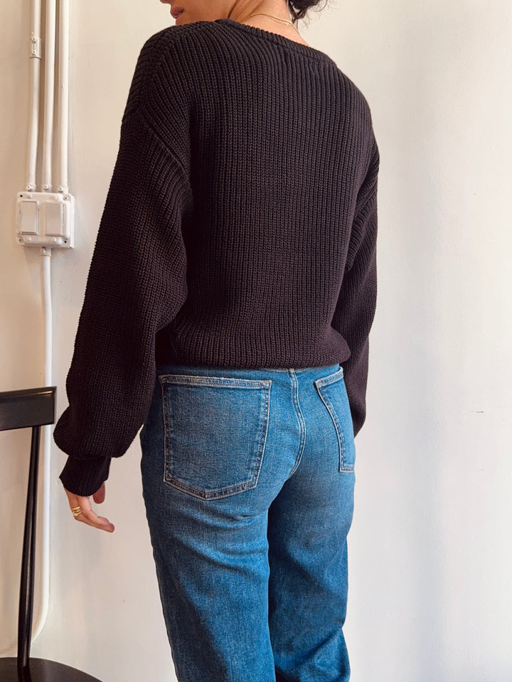 Person wearing a dark sweater and blue jeans against a plain background