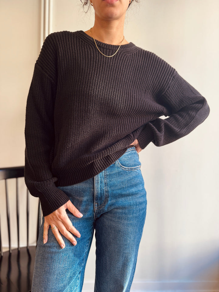 Person wearing a dark sweater and blue jeans against a neutral background winsome chicago cute boutique