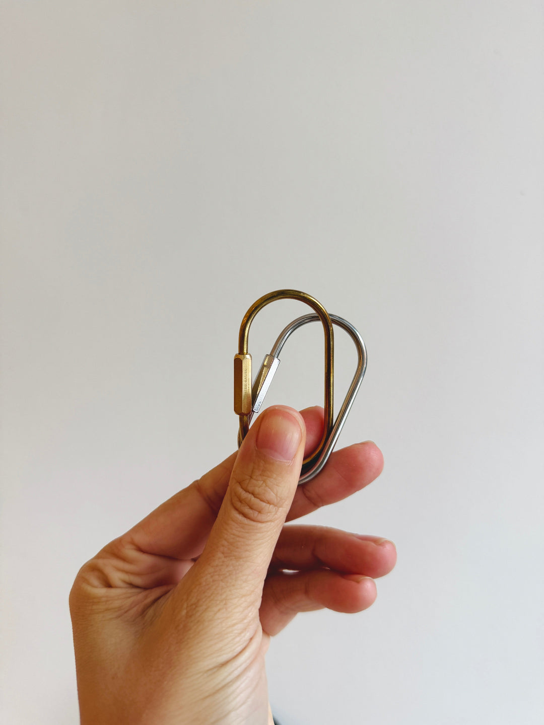 Hand holding a metal carabiner against a plain background