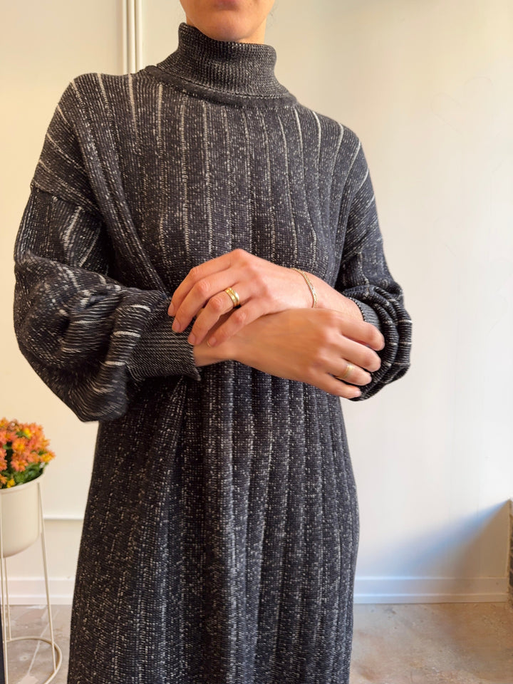 Person wearing a long dark gray ribbed sweater in a minimal indoor setting.
