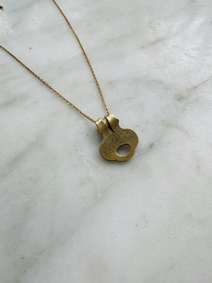 Brass key-shaped pendant on a chain against a marble background