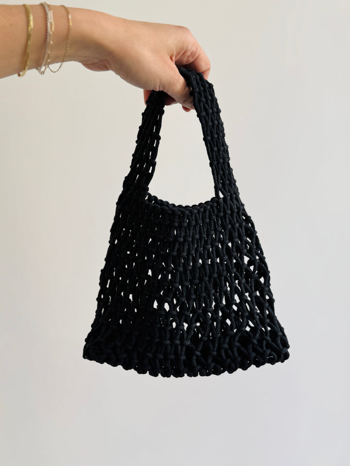 a hand holding a woven cotton handbag by the handle. Small handbag perfect for events in the spring summer and fall.