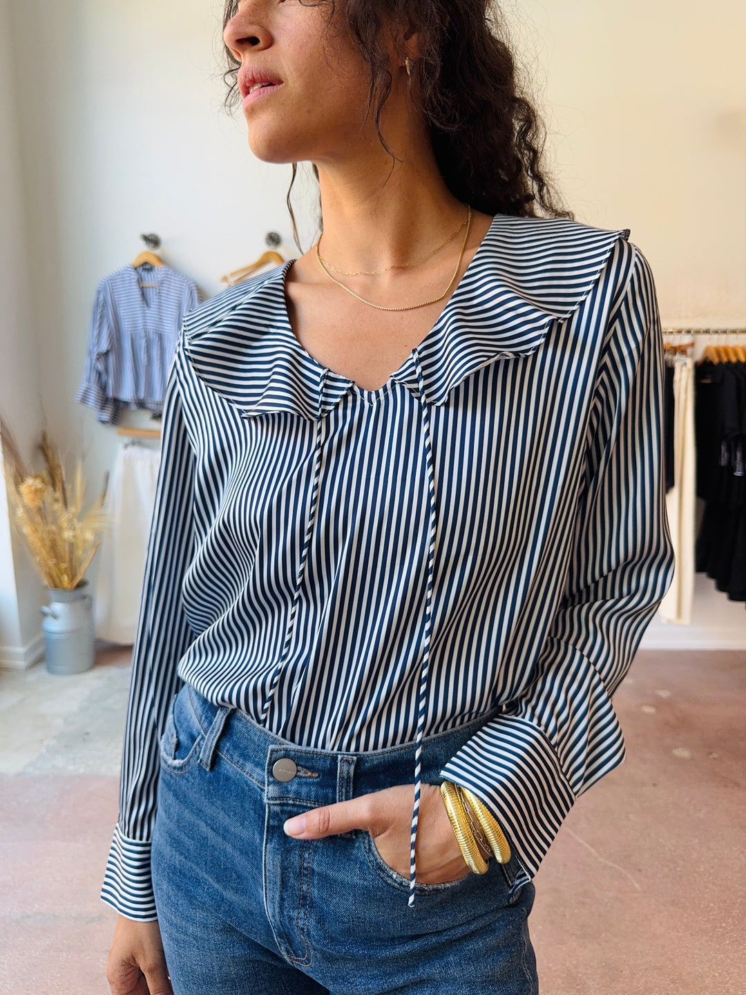 Woman wearing a black and white striped shirt with a flouncy collar and cuffed sleeves in a clothing store.