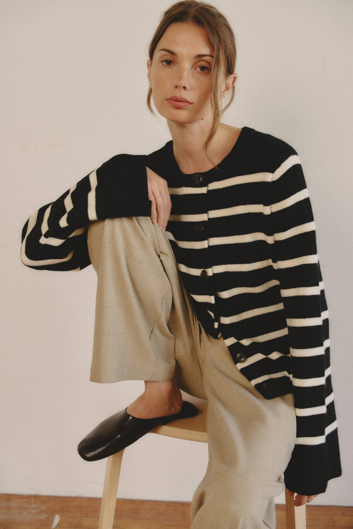 Woman wearing a black and white striped sweater and beige pants sitting on a stool.