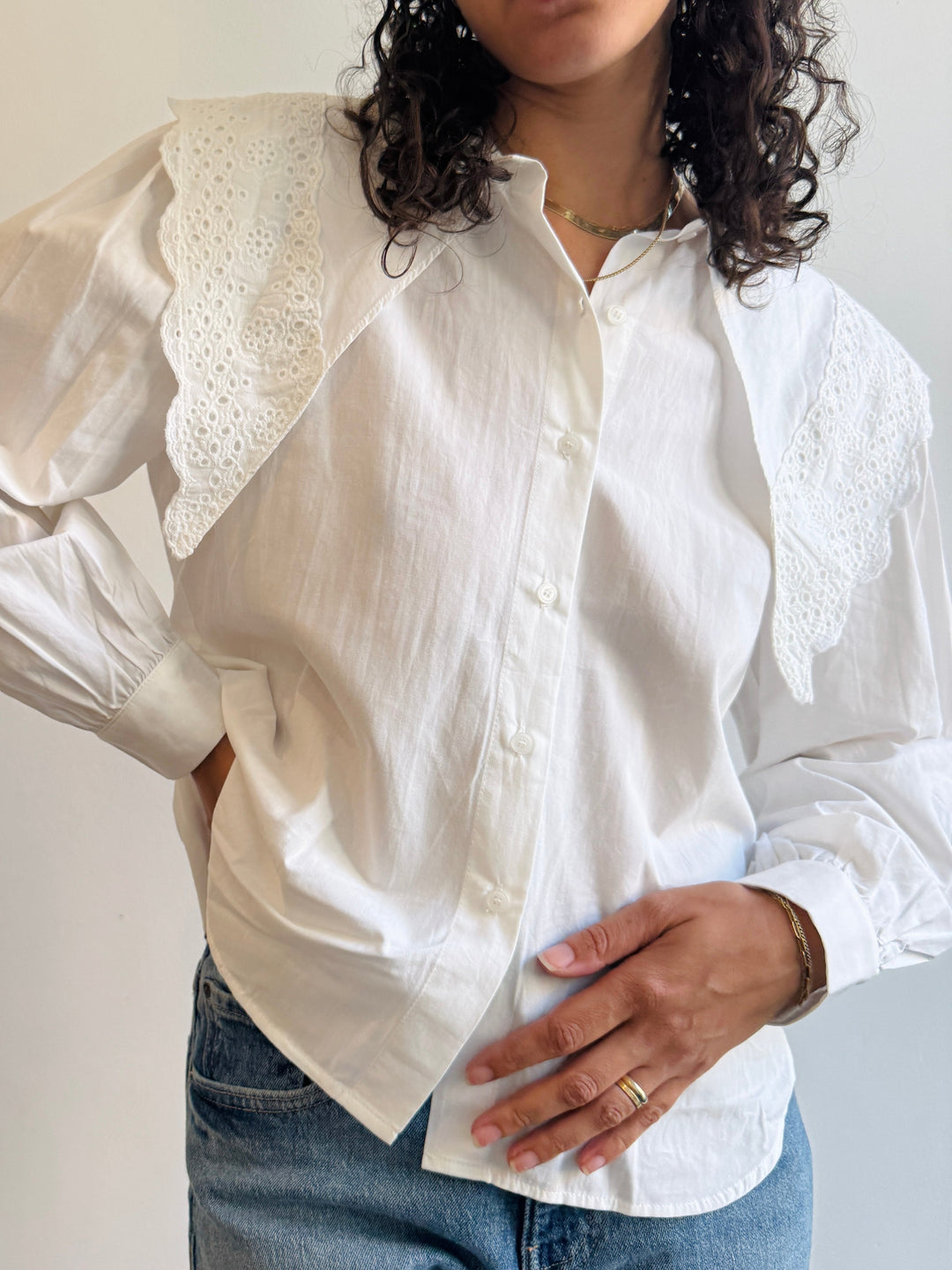 Woman wearing a white cotton shirt with large long exaggerated collar with cotton lace details.