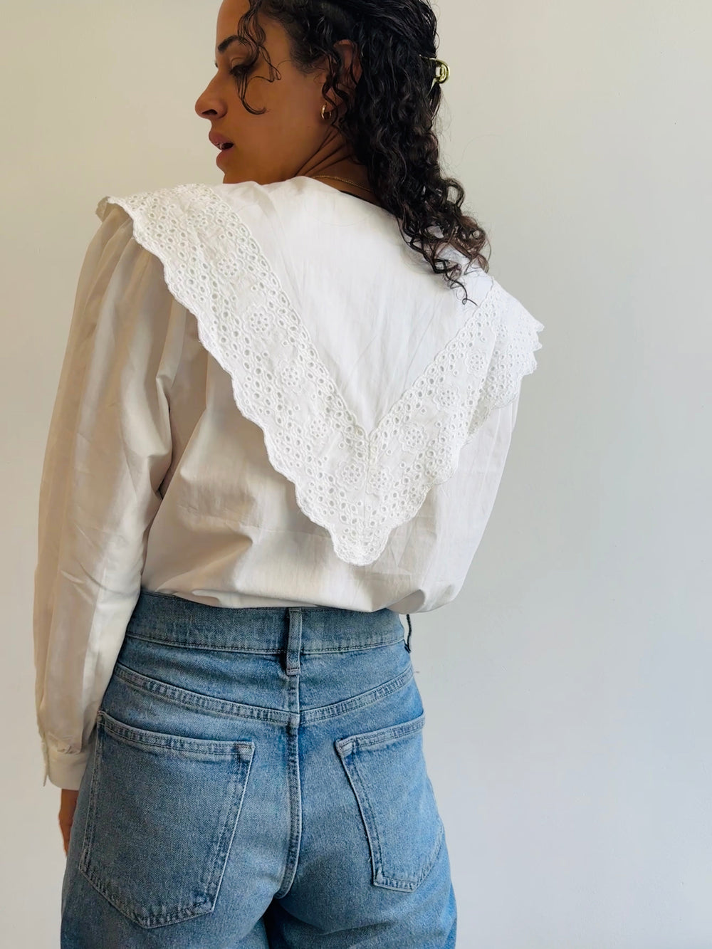 the back of a woman wearing a white cotton exaggerated collared shirt that comes down to a point in the back.