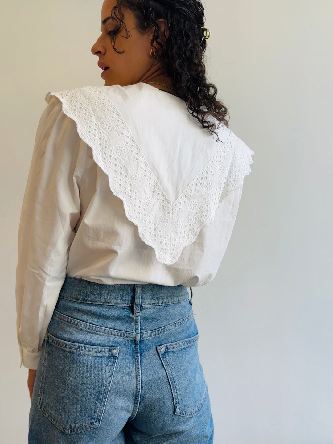 the back of a woman wearing a white cotton exaggerated collared shirt that comes down to a point in the back.