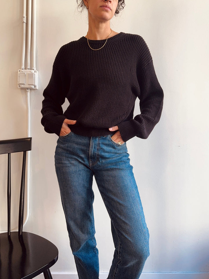 Person wearing a black sweater and blue jeans against a white wall. winsome boutique chicago