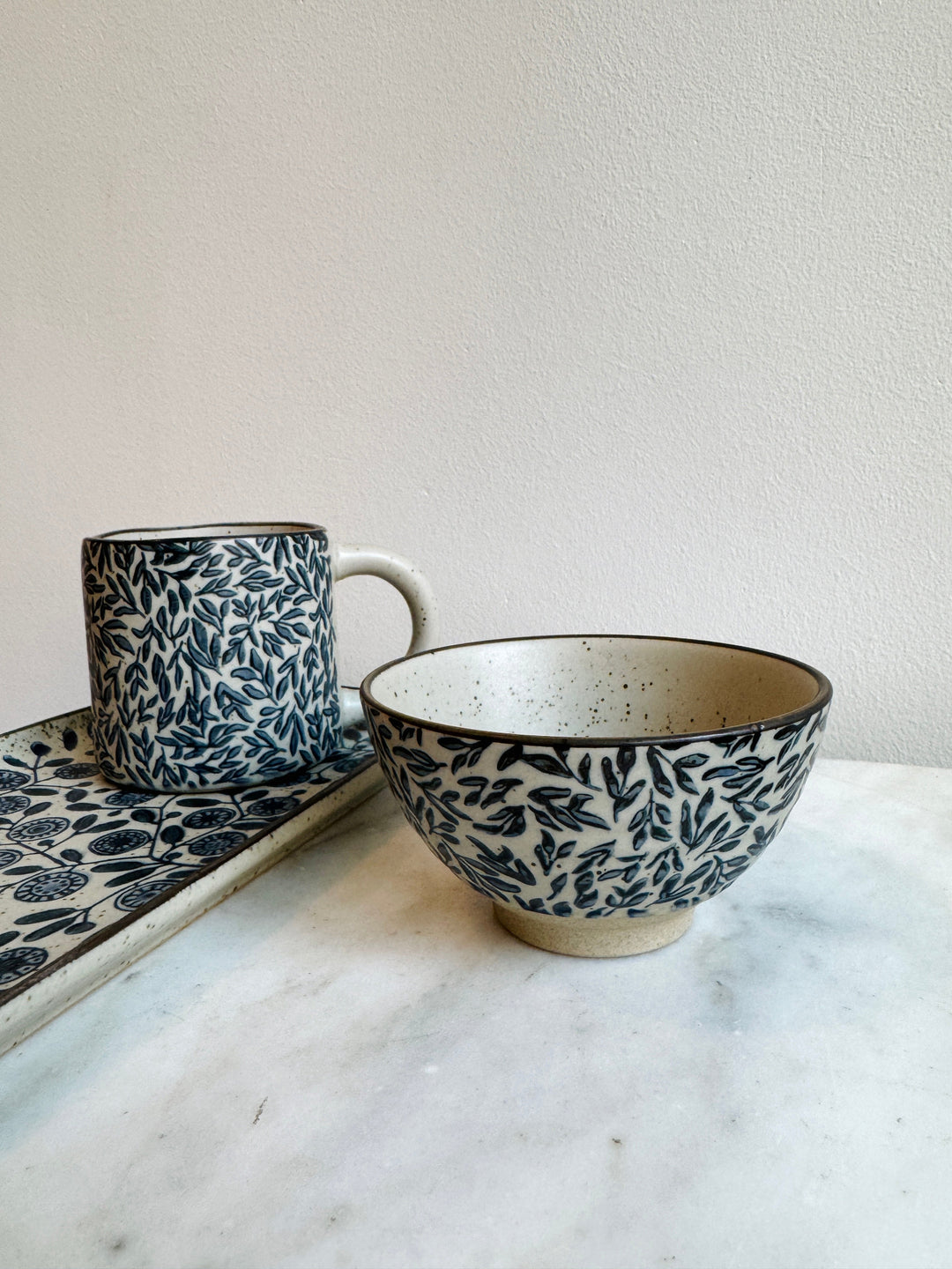 Ceramic mug and bowl with navy blue leaf pattern on a marble surface