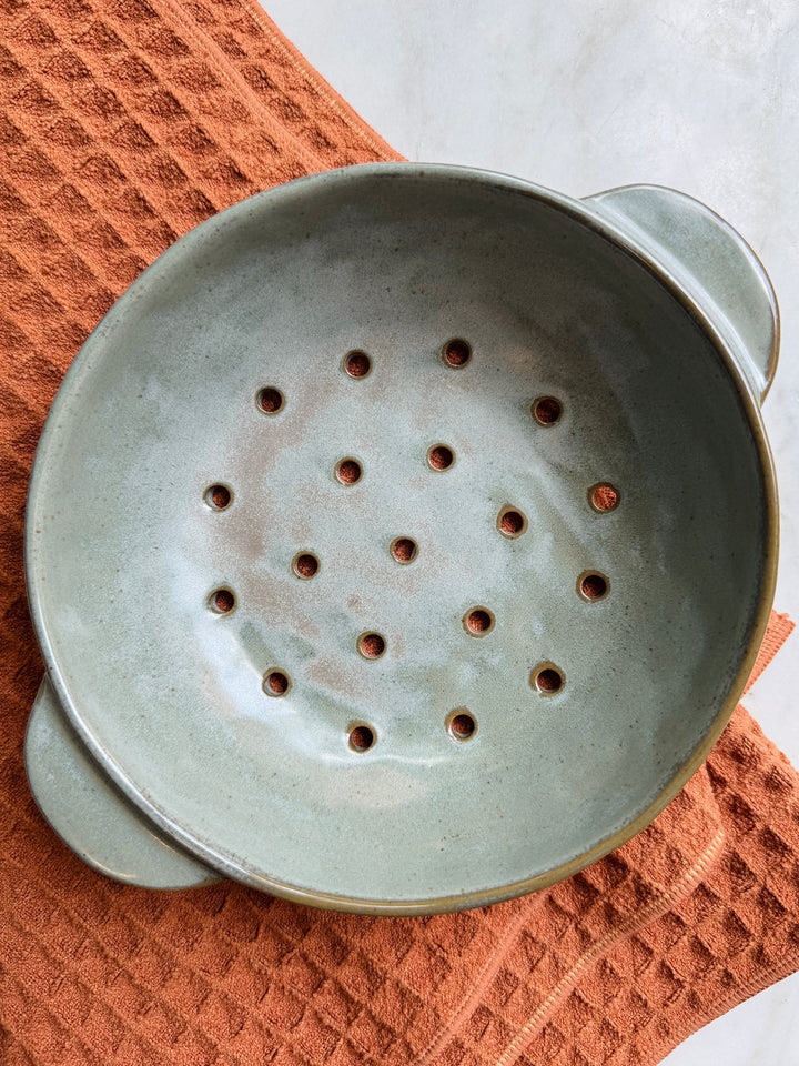Ceramic colander on a textured orange surface