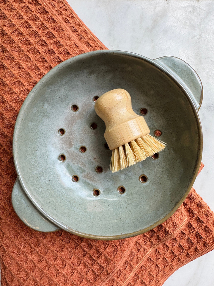 Gray ceramic strainer with wooden brush on a textured orange towel