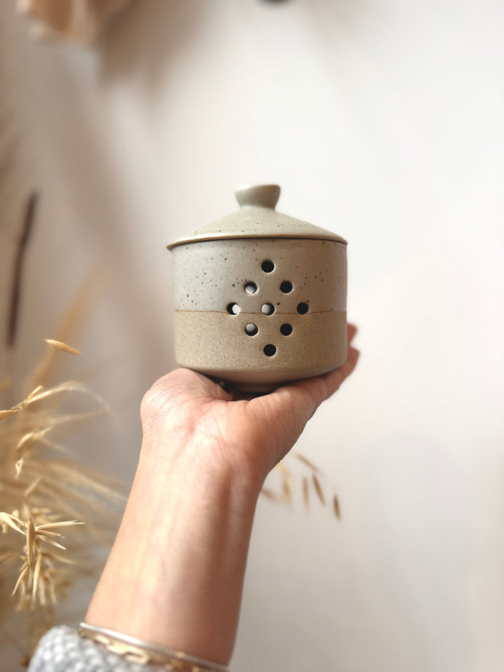 Hand holding a ceramic garlic kepper with a blurred background