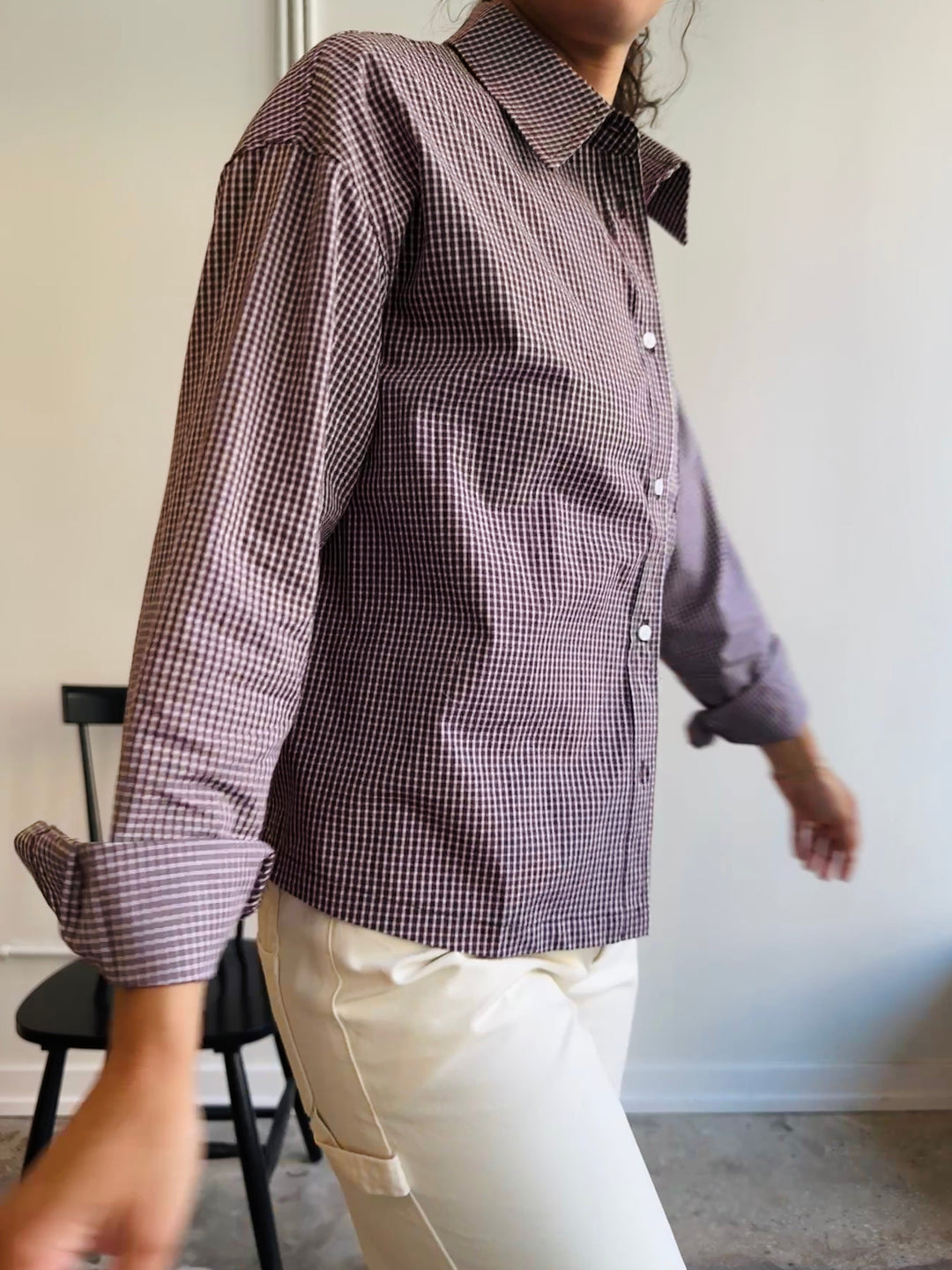 Person wearing a checkered shirt with rolled-up sleeves in an indoor setting