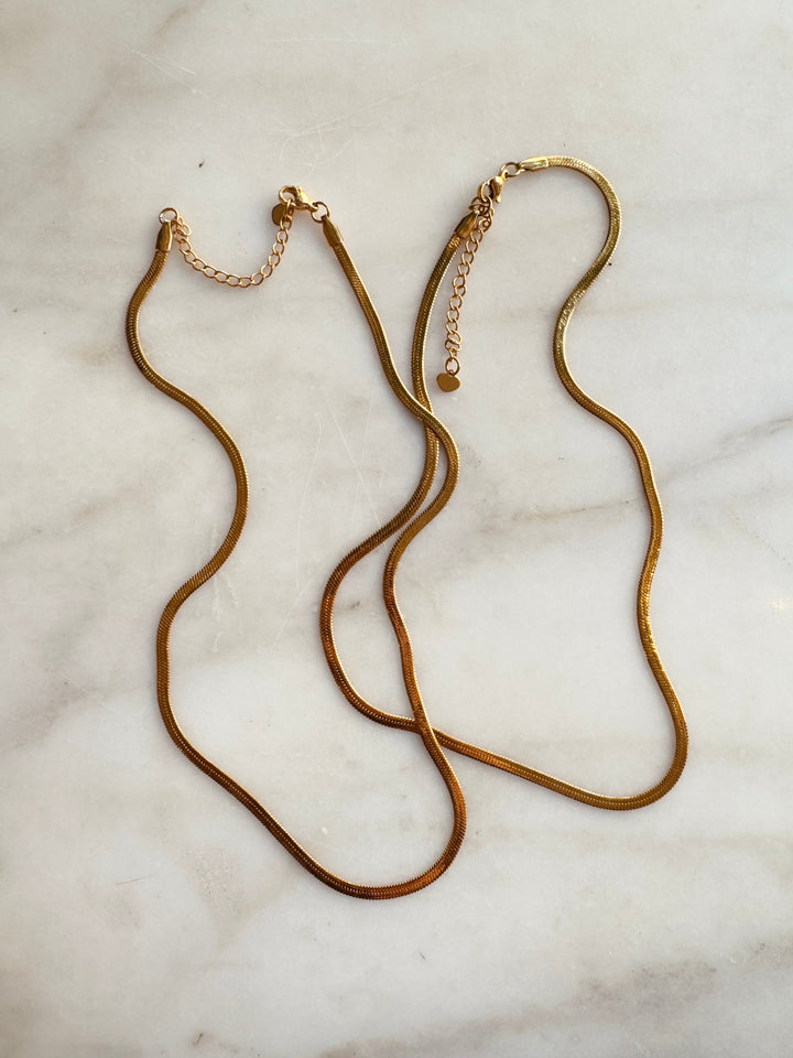two herringbone gold filled chains on a white marble surface at winsome clothing and goods chicago boutique avondale