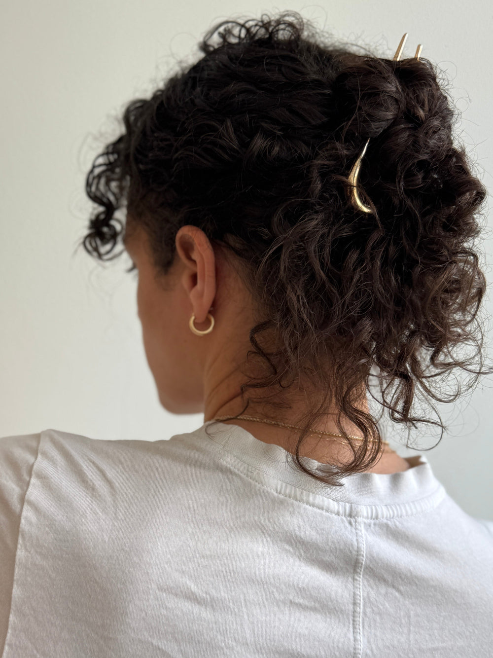 Person with messy bun curly hair wearing a white top and gold french hair pin against a neutral background