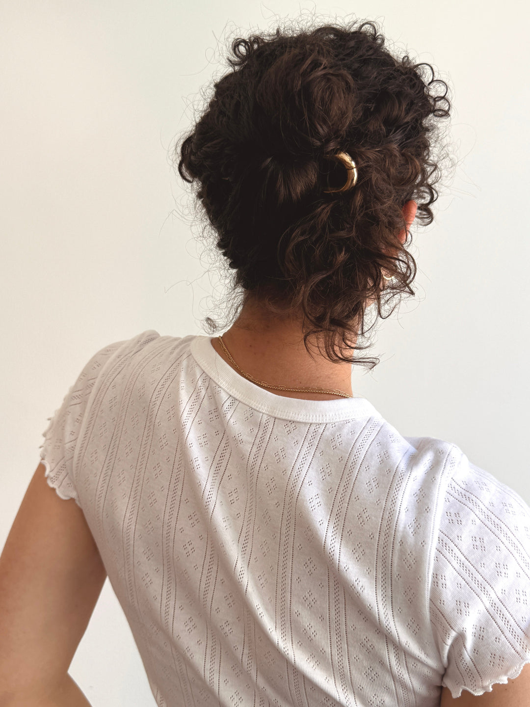Person wearing a white pointelle lace top with a gold hair pin in curly chignon bun