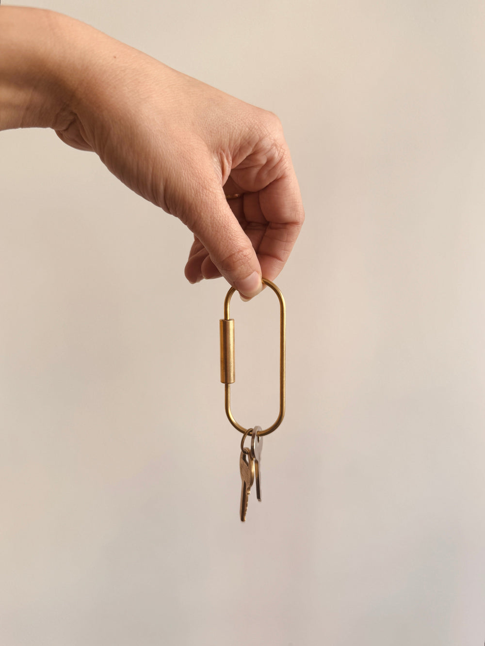 Hand holding a brass keychain with keys against a plain background