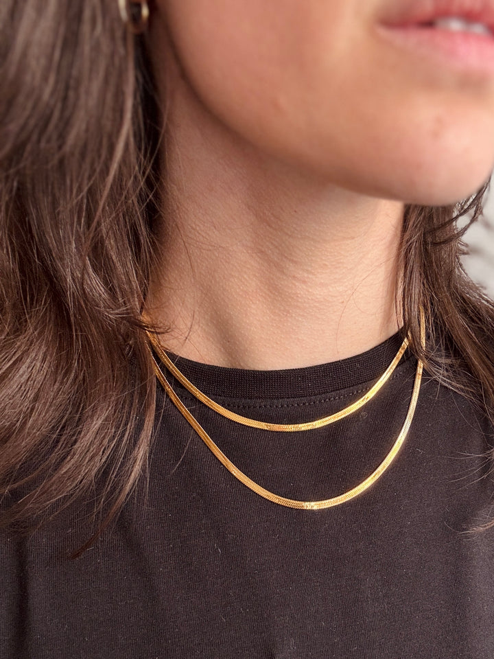 Close-up of a person wearing a gold necklace against a blurred background from Winsome clothing and goods a cute boutique in avondale chicago
