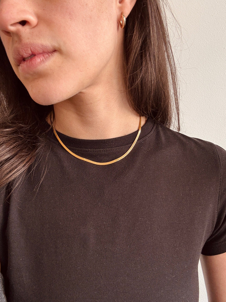 Close-up of a person wearing a gold necklace against a neutral background from Winsome clothing and goods a cute boutique in avondale chicago