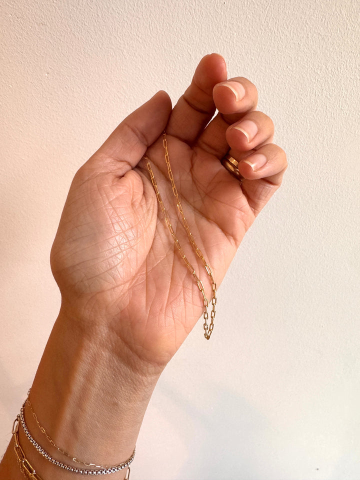 Hand holding a gold chain necklace against a plain background