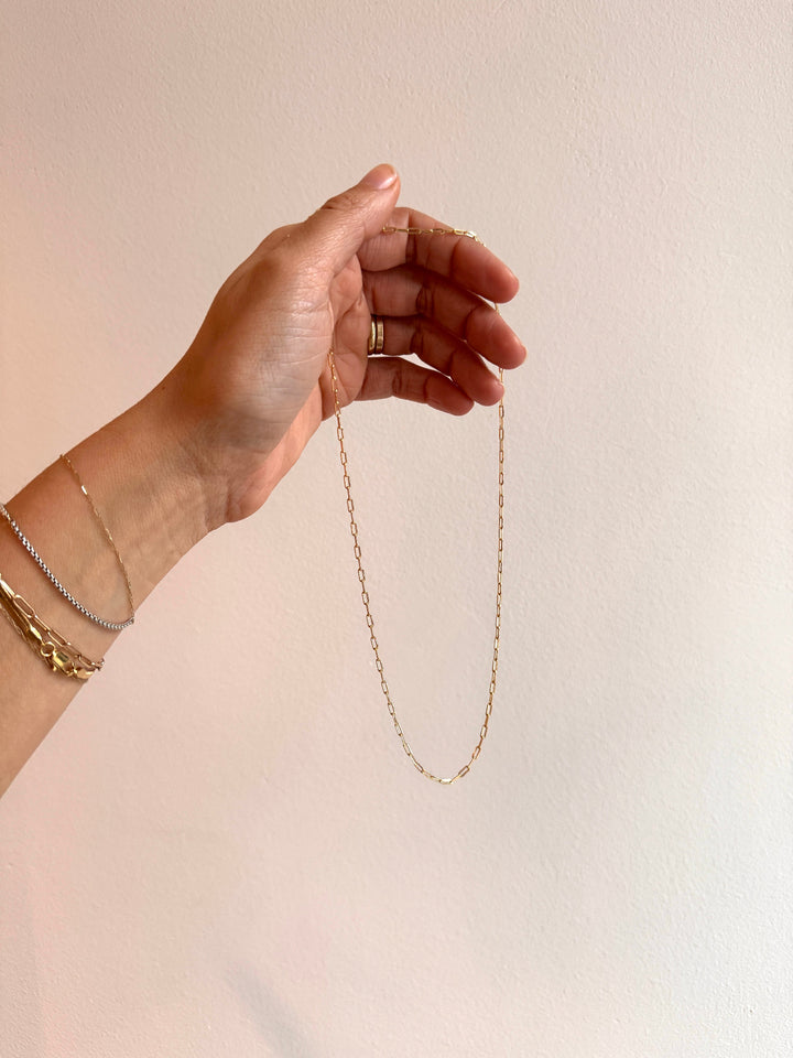 Hand holding a gold chain necklace against a plain background