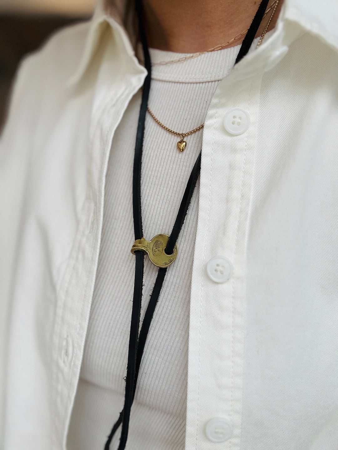 Close-up of a person wearing a white shirt with a bolo tie and necklace.