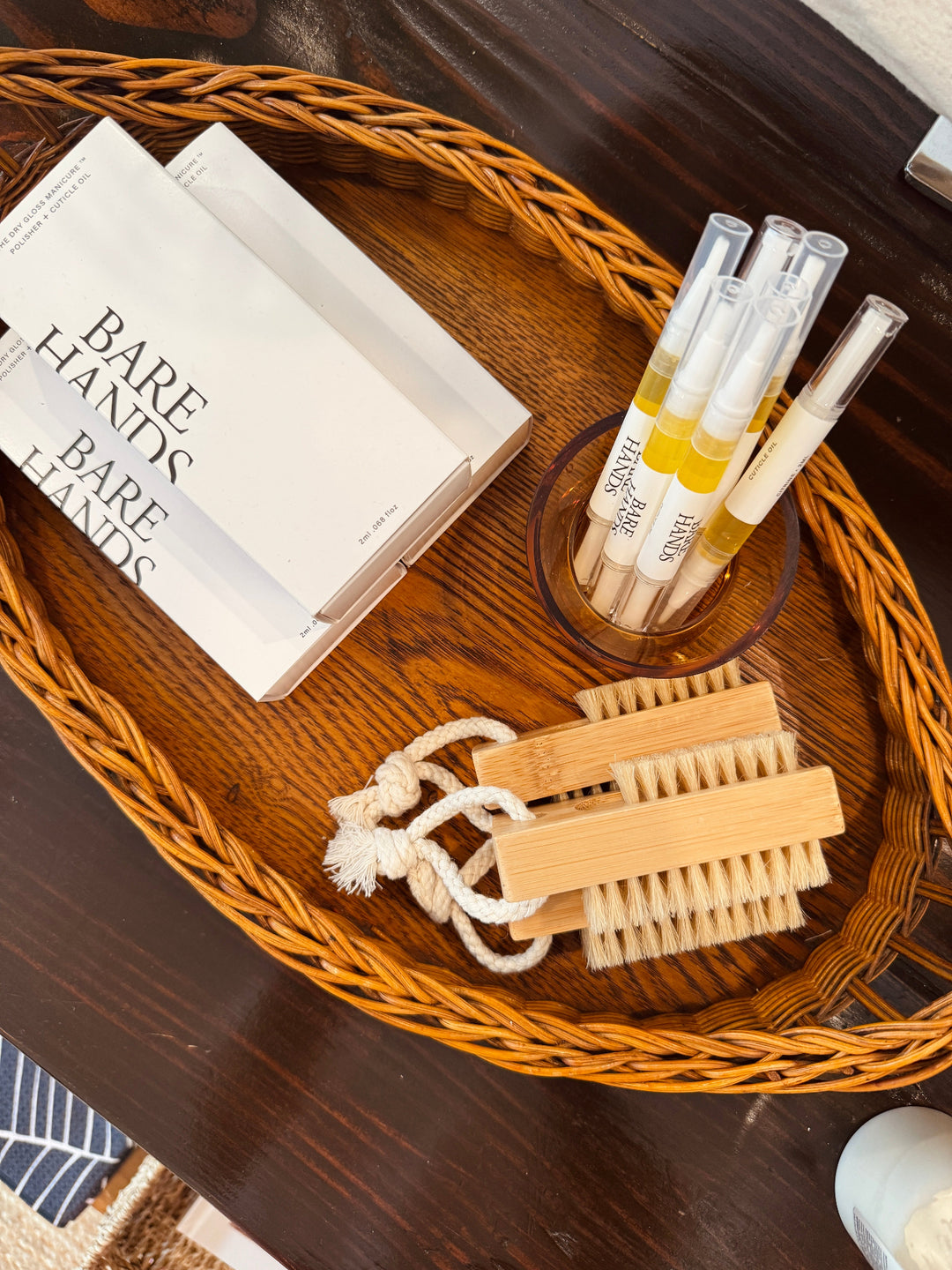 Wooden tray with 'Bare Hands' products including nail brushes and a cuticle oils on a wooden table.