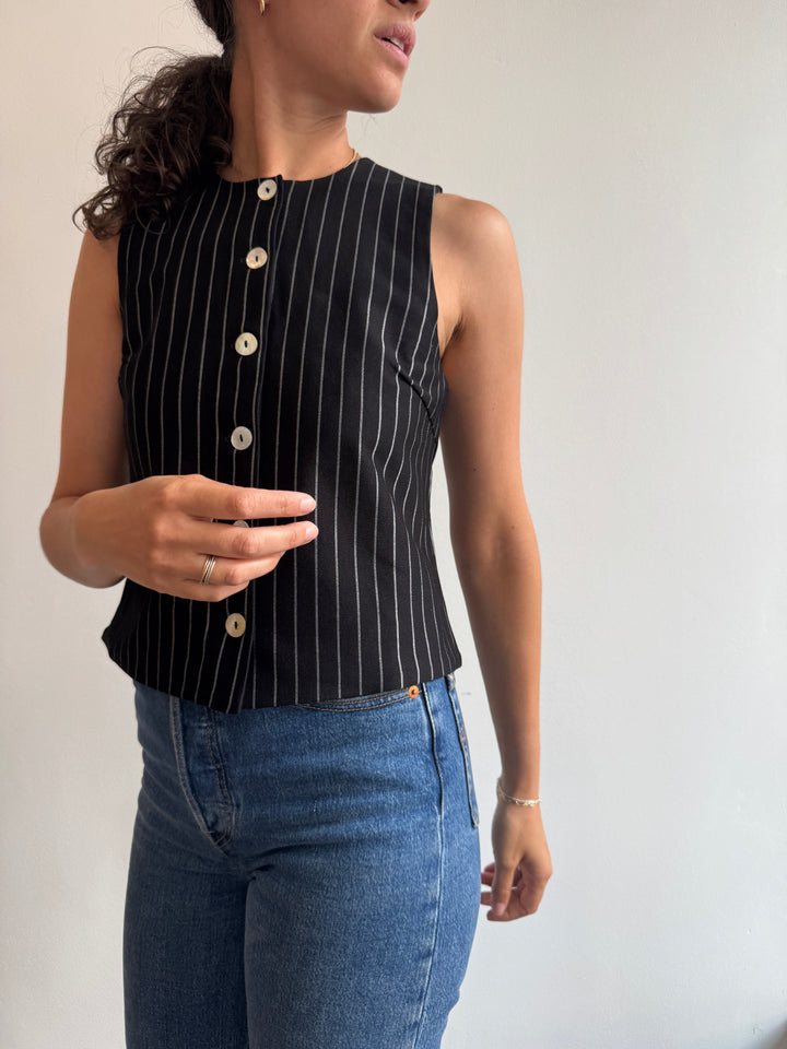 Person wearing a black pinstripe top with white buttons and blue jeans on a light background