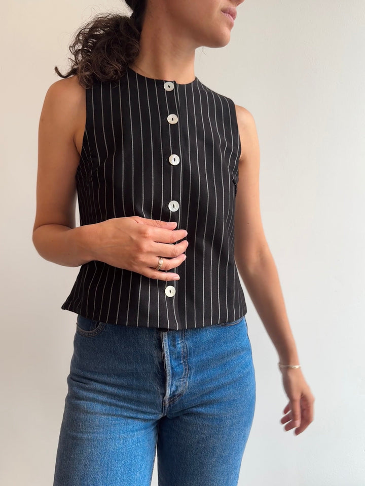 Person wearing a black pinstripe sleeveless top and blue jeans against a plain background