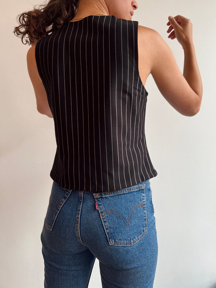 Person wearing a black pinstripe sleeveless top and blue jeans on a plain background