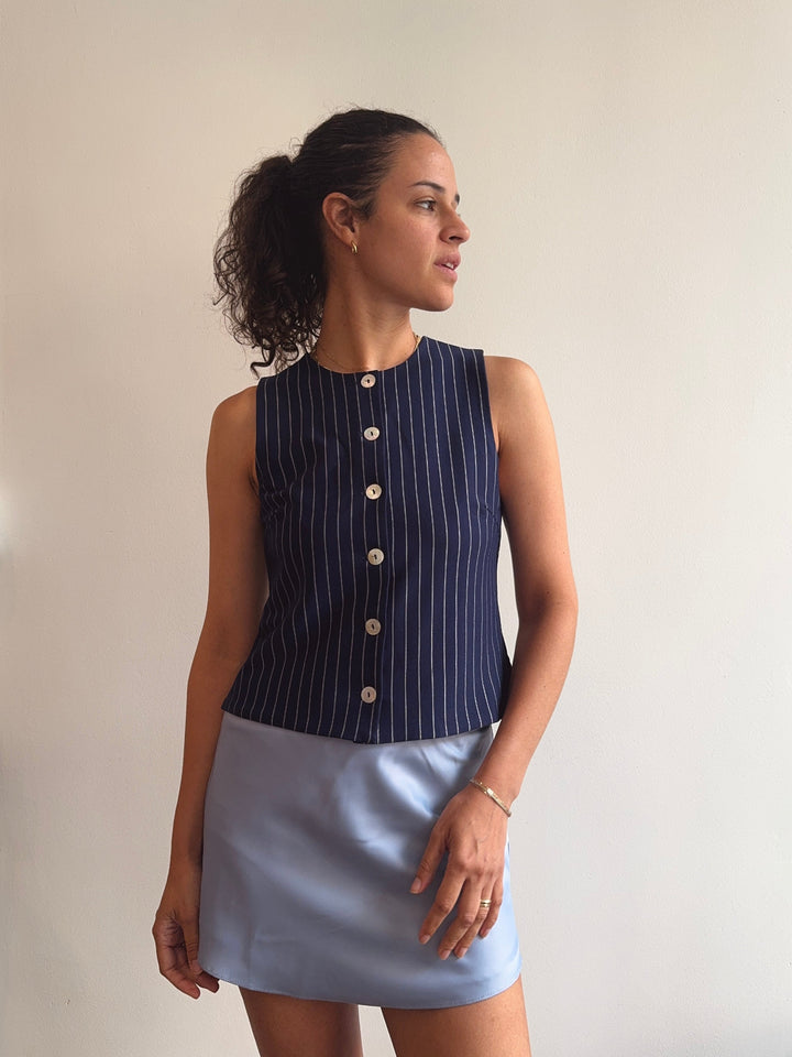Woman wearing a navy pinstripe sleeveless top and light blue skirt against a plain background