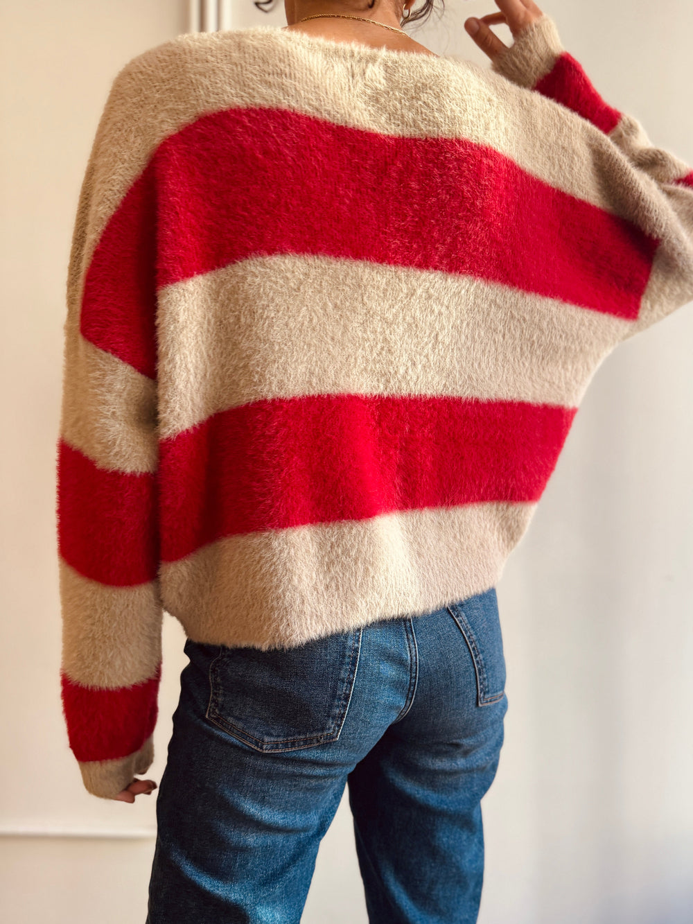 Person wearing a red and beige striped sweater with blue jeans against a neutral background