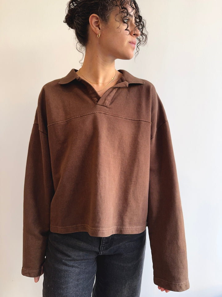 Person wearing a brown rugby sweatshirt against a plain background