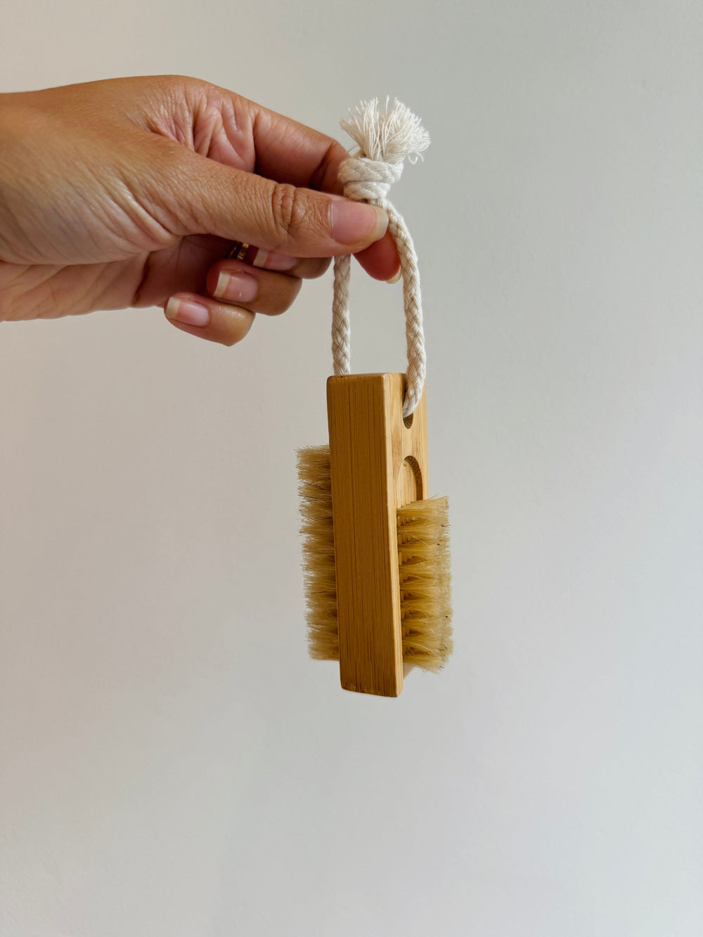 Hand holding a wooden brush with bristles against a plain background