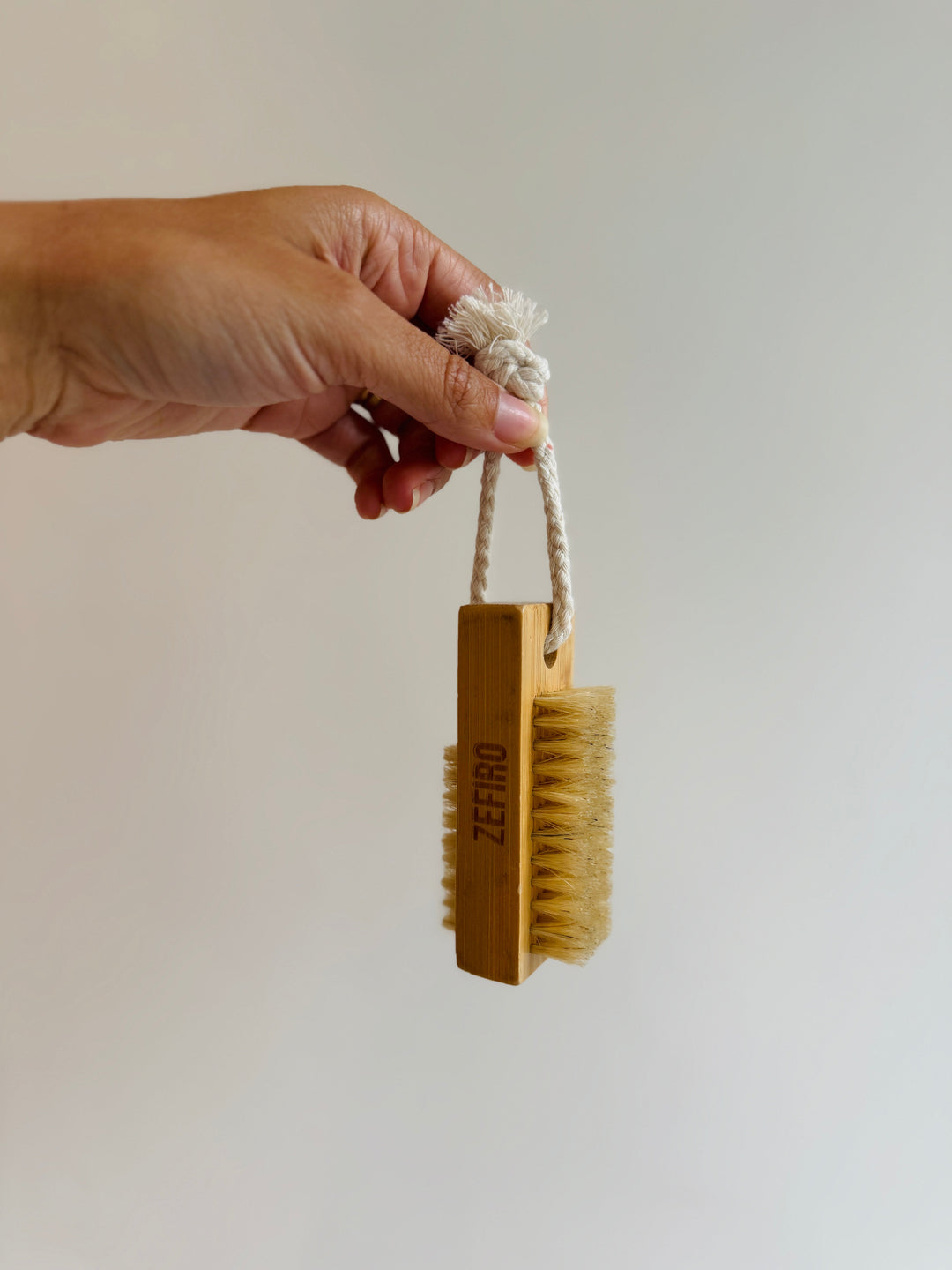 Hand holding a wooden brush with a rope handle against a plain background
