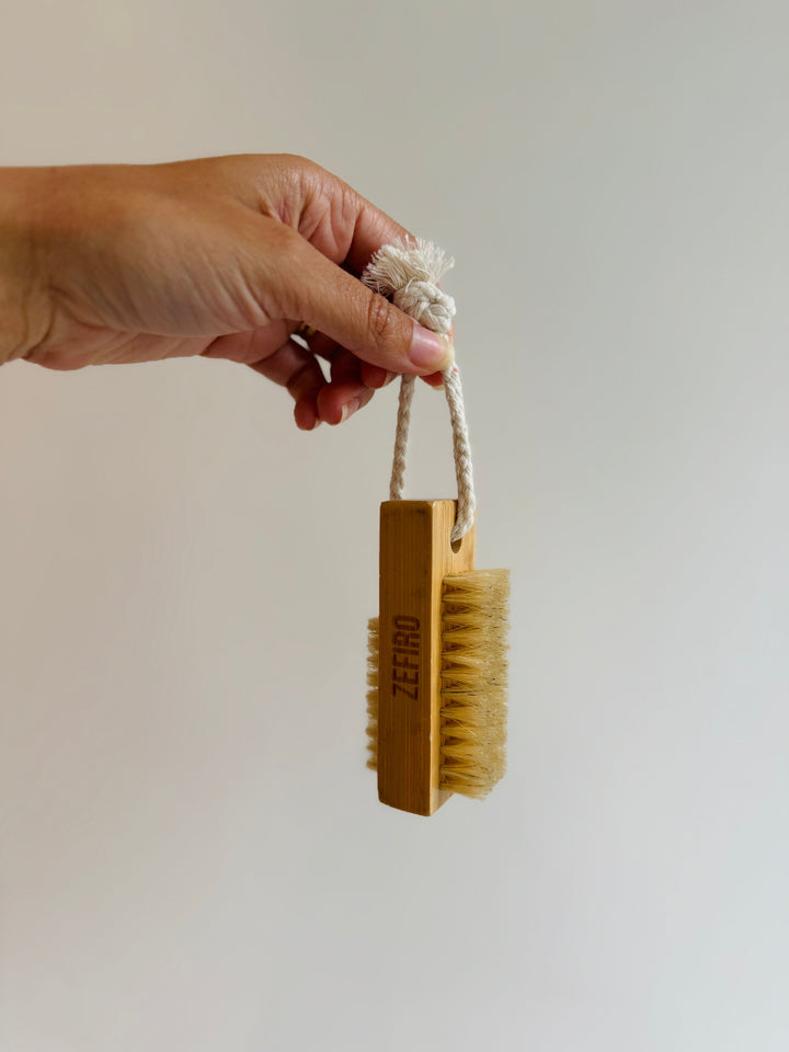 Hand holding a wooden brush with a rope handle against a plain background