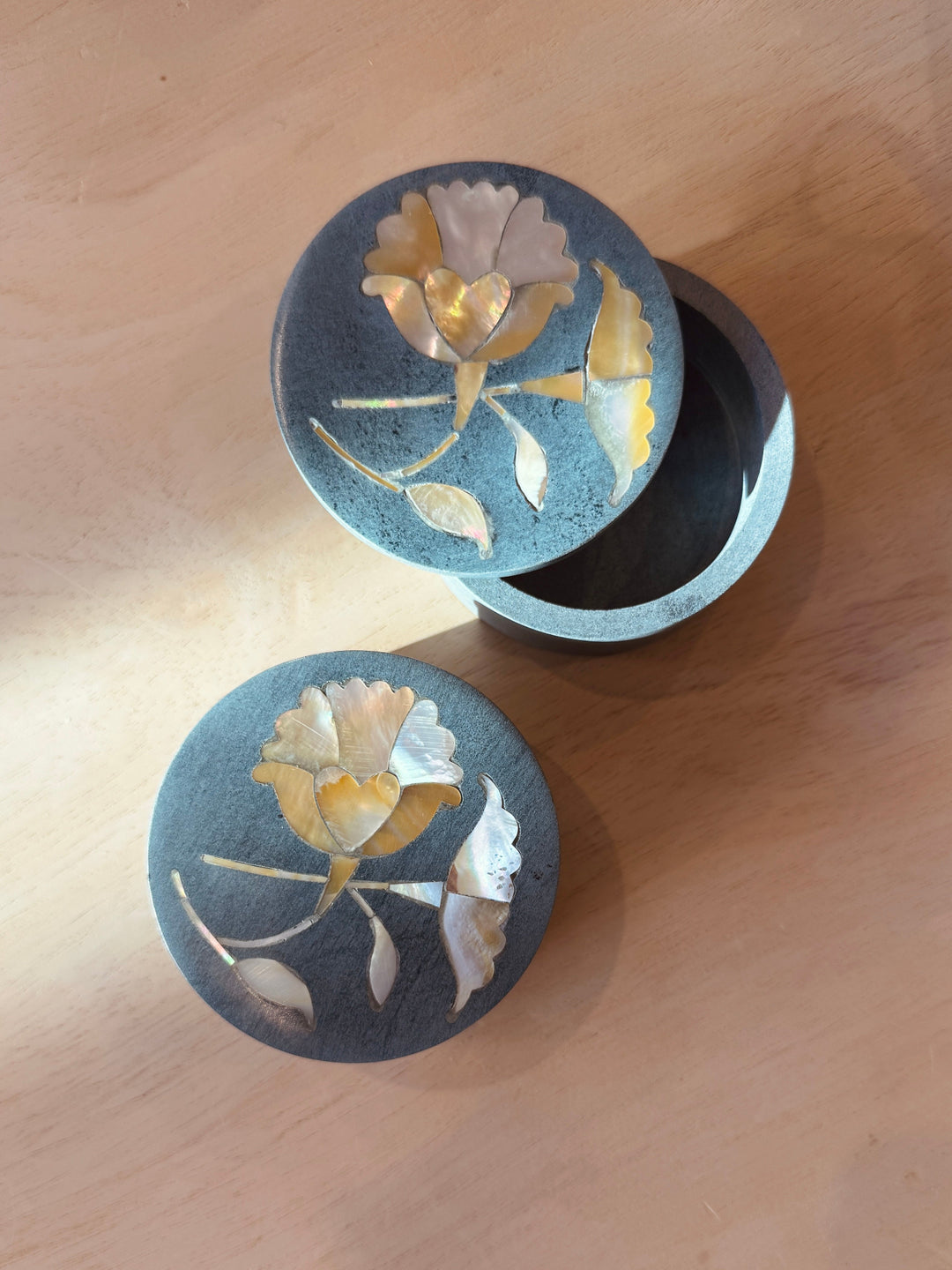 Two round decorative stone boxes with floral designs on a wooden surface