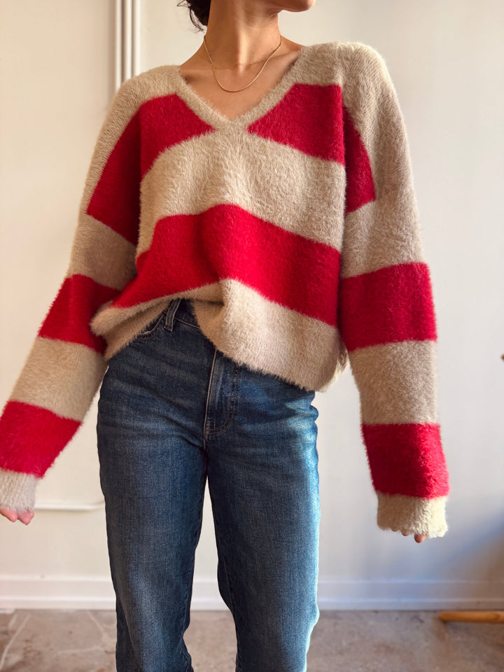 Person wearing a red and beige striped sweater with blue jeans against a neutral background